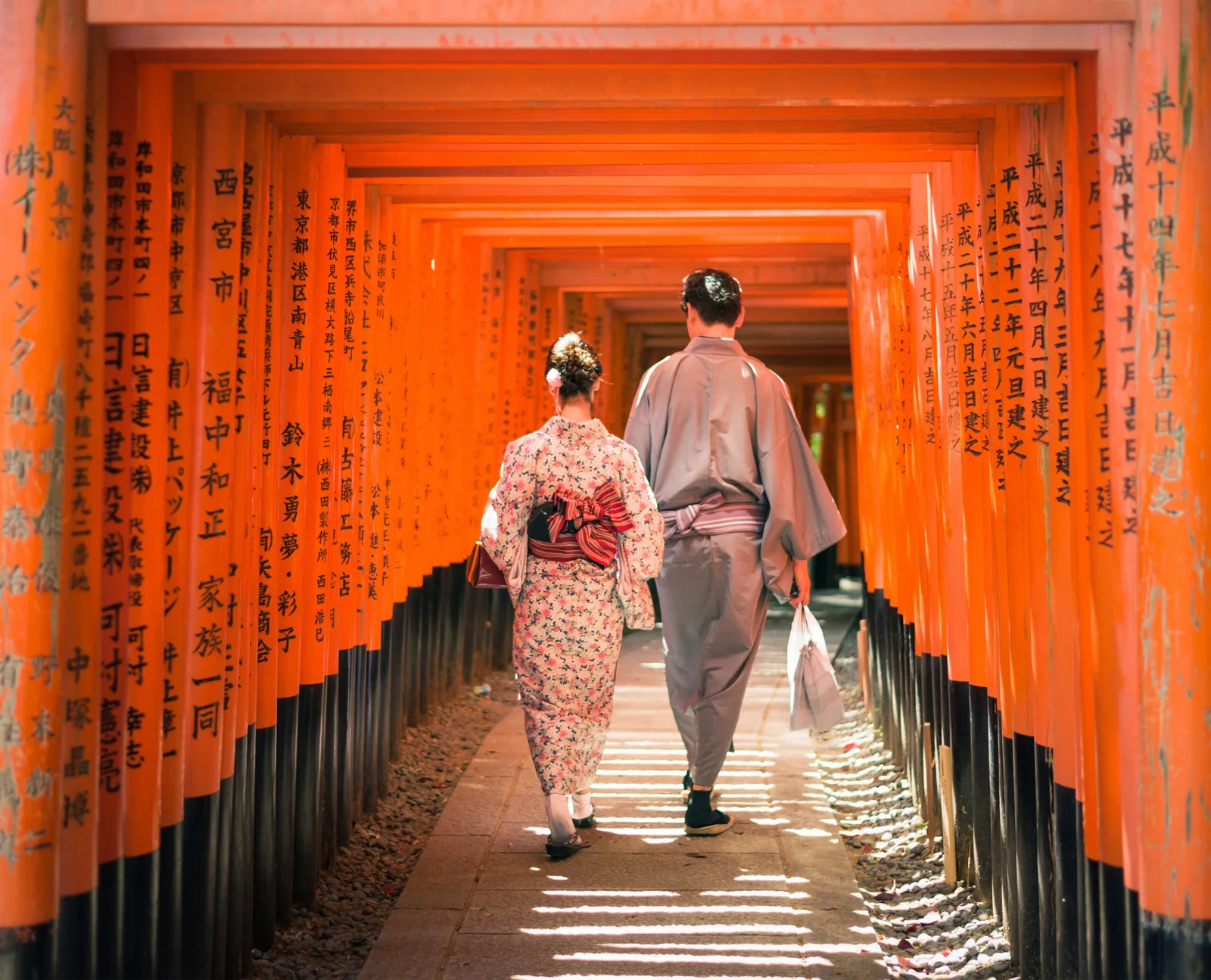 Kyoto, Japan – May 11, 2015: A couple wearing traditional Japanese kimonos, walking through a long series of inscribed Torii gates at Fushimi Inari-Taisha, on the outskirts of the ancient Japanese city of Kyoto.